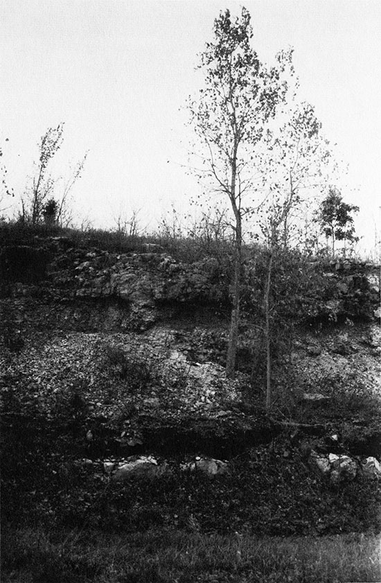 Black and white photo of rocks exposed when hill is cut for road construction.
